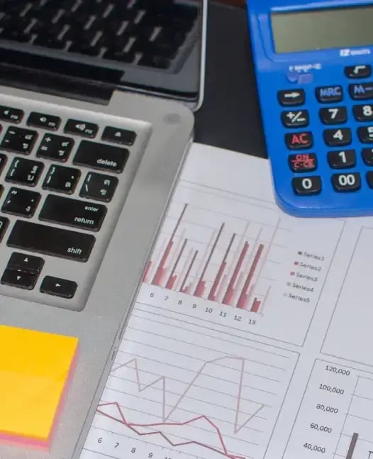 Laptop, calculator, and printed financial reports with visible charts and data tables, illustrating financial reporting tasks.