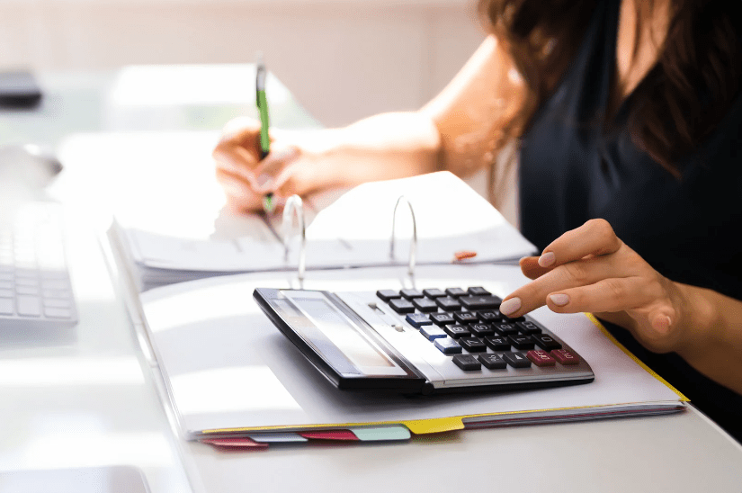 A chartered accountant hand calculating tax for a business while writing in a ring binder to help avoid them from making a mistake. 