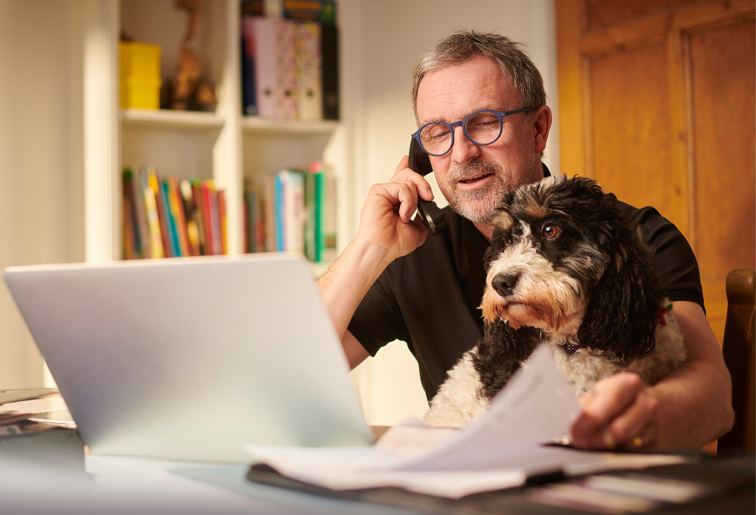 Small business owner working from home, reviewing paperwork on a laptop while speaking on the phone, illustrating Making Tax Digital compliance. 